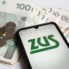 ZUS na ekranie telefonu obok polskich banknotów i monet. Symbolizuje to świadczenia związane z częściową niezdolnością do pracy.