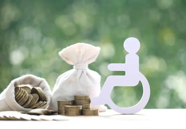 Symbol osoby na wózku inwalidzkim obok worków z pieniędzmi i monet. Zastanawiasz się, ile wynosi zasiłek dla osób niepełnosprawnych?
