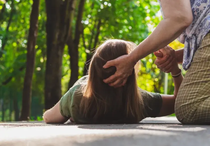 Osoba na ziemi, być może doświadczająca nietypowych objawów padaczki, otrzymuje pomoc od drugiej osoby.