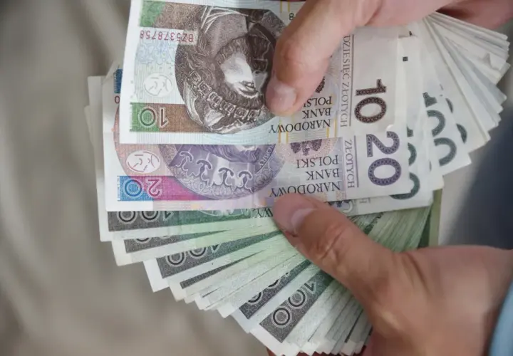 Dłonie trzymają plik polskich banknotów 10, 20 i 100 zł. To wsparcie finansowe, które może być świadczeniem wspierającym dla osób niepełnosprawnych.