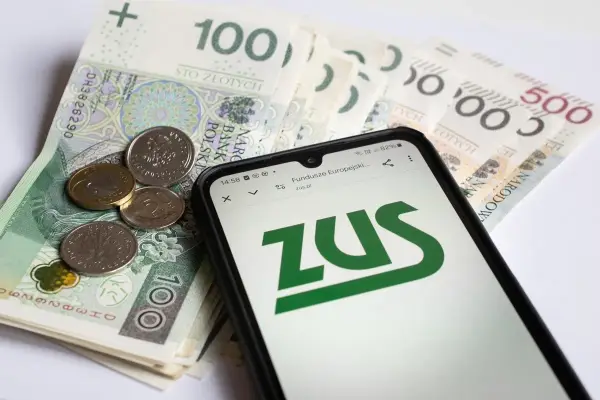 ZUS na ekranie telefonu obok polskich banknotów i monet. Symbolizuje to świadczenia związane z częściową niezdolnością do pracy.